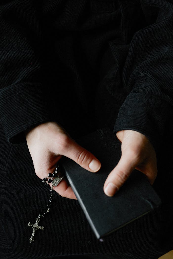 Close-up of hands holding a prayer book and rosary beads, symbolizing faith and spirituality.
